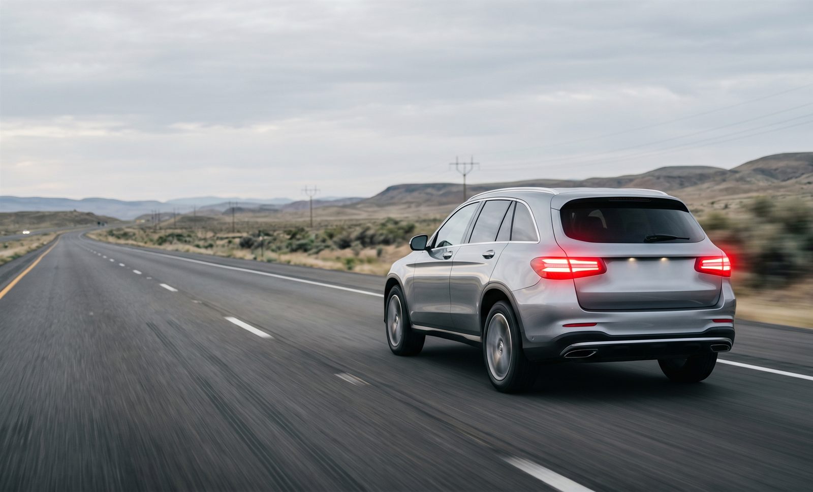 A silver SUV driving down an open highway with its brake lights illuminated